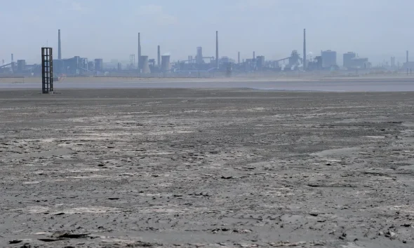 a body of water with a layer of solid matter on its surface with industrial facilities in the backgr