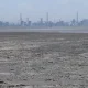 a body of water with a layer of solid matter on its surface with industrial facilities in the backgr