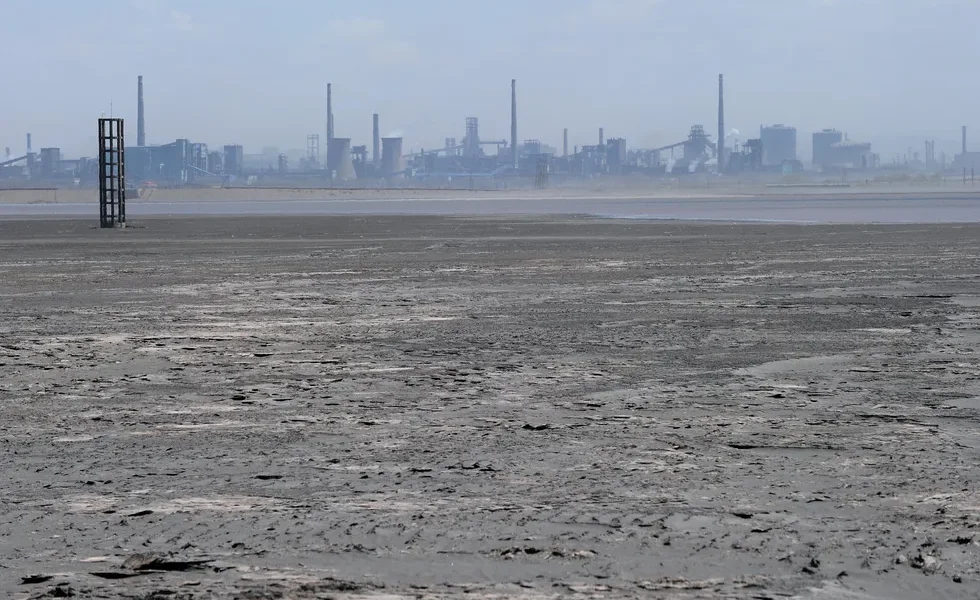 a body of water with a layer of solid matter on its surface with industrial facilities in the backgr