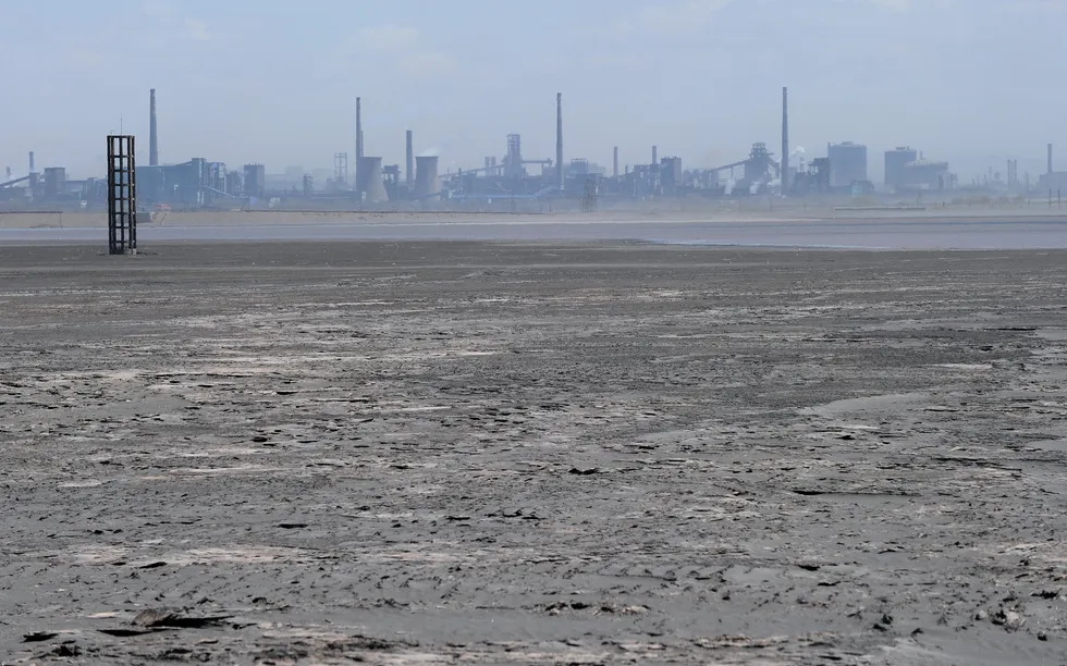 a body of water with a layer of solid matter on its surface with industrial facilities in the backgr