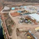 an aerial view of a complex of industrial buildings and large aboveground tanks near a large artific