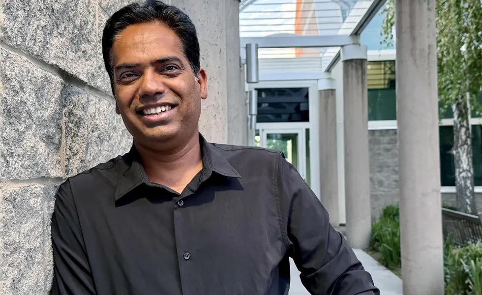 an indian man in a dress shirt smiling in front of the entrance to an office building