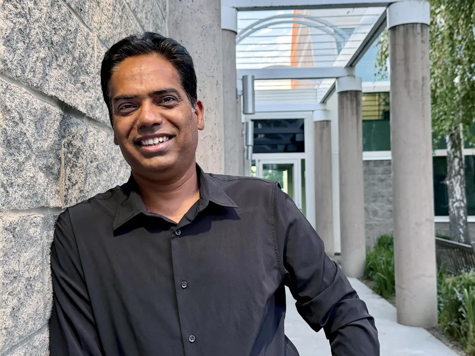 an indian man in a dress shirt smiling in front of the entrance to an office building
