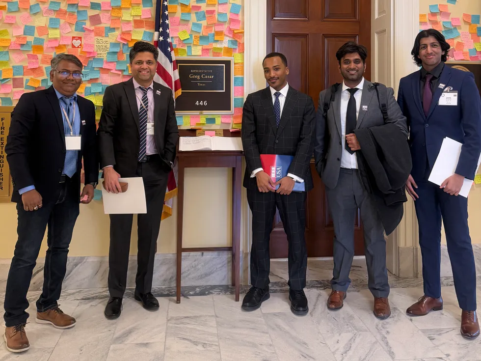 group of five men standing outside an office with a placard that reads representative greg casar