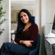 smiling portrait of a young south asian woman seated in front of her work computer