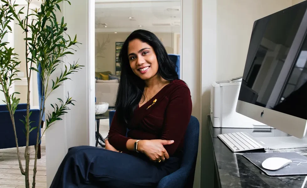 smiling portrait of a young south asian woman seated in front of her work computer