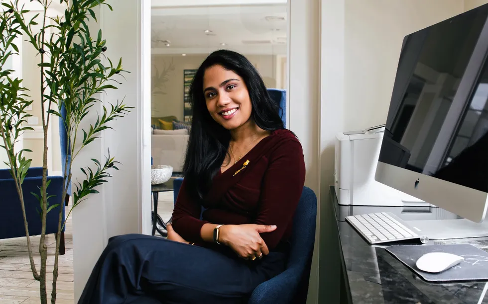 smiling portrait of a young south asian woman seated in front of her work computer