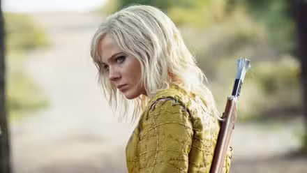 Freya Allan with a weapon on her back looks at someone off-camera in The Witcher Season 4